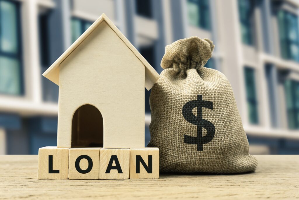 Miniature house with 'Loan' written in Scrabble pieces in front of it.